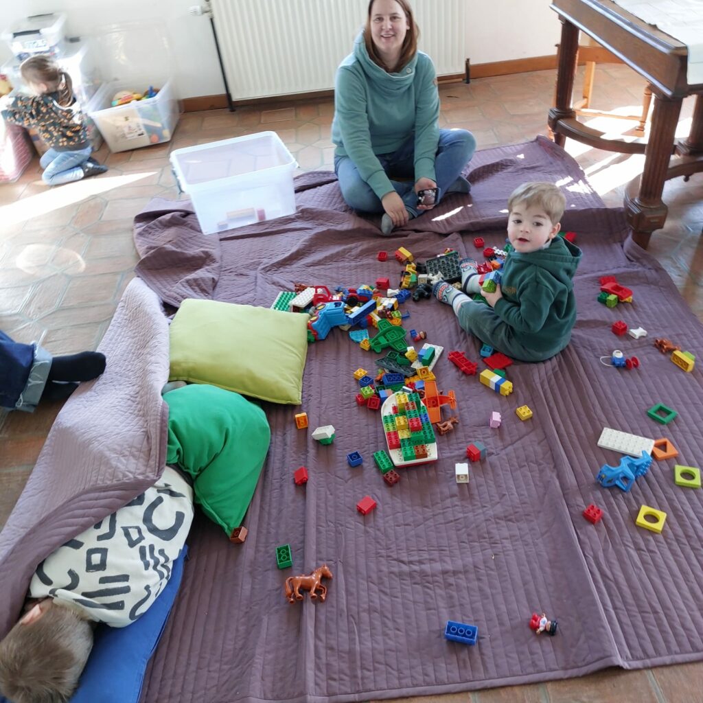 une jeune femme qui joue au lego avec un petit garçon. Ils sont assis sur le sol