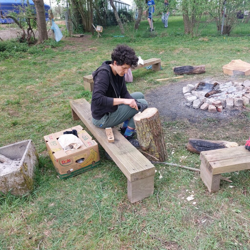 Une femme près d'un feu taille un morceau de bois