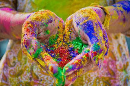 Une personne tient dans ses mains des pigments de couleur vives, ses mains et ses bras en sont tachés