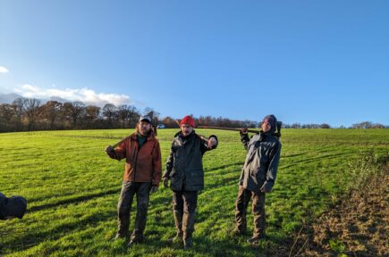 Dans un champs, trois hommes avec des houe-hâche