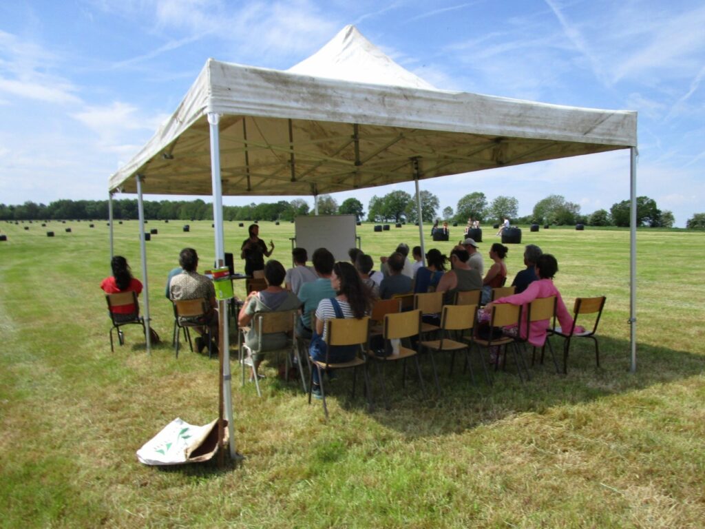 Un groupe de personnes assistant à une conférence sous une tonnelle en plen milieu d'un champs