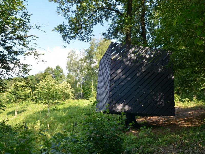 Une oeuvre de land Art. Une grand cube fait avec des lattes de bois mises en oblique.