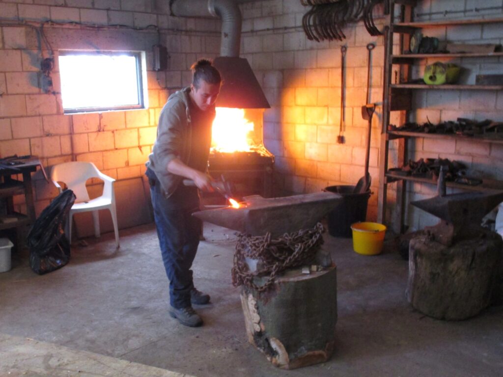 un forgeron forge un outil avec son marteau et son enclume