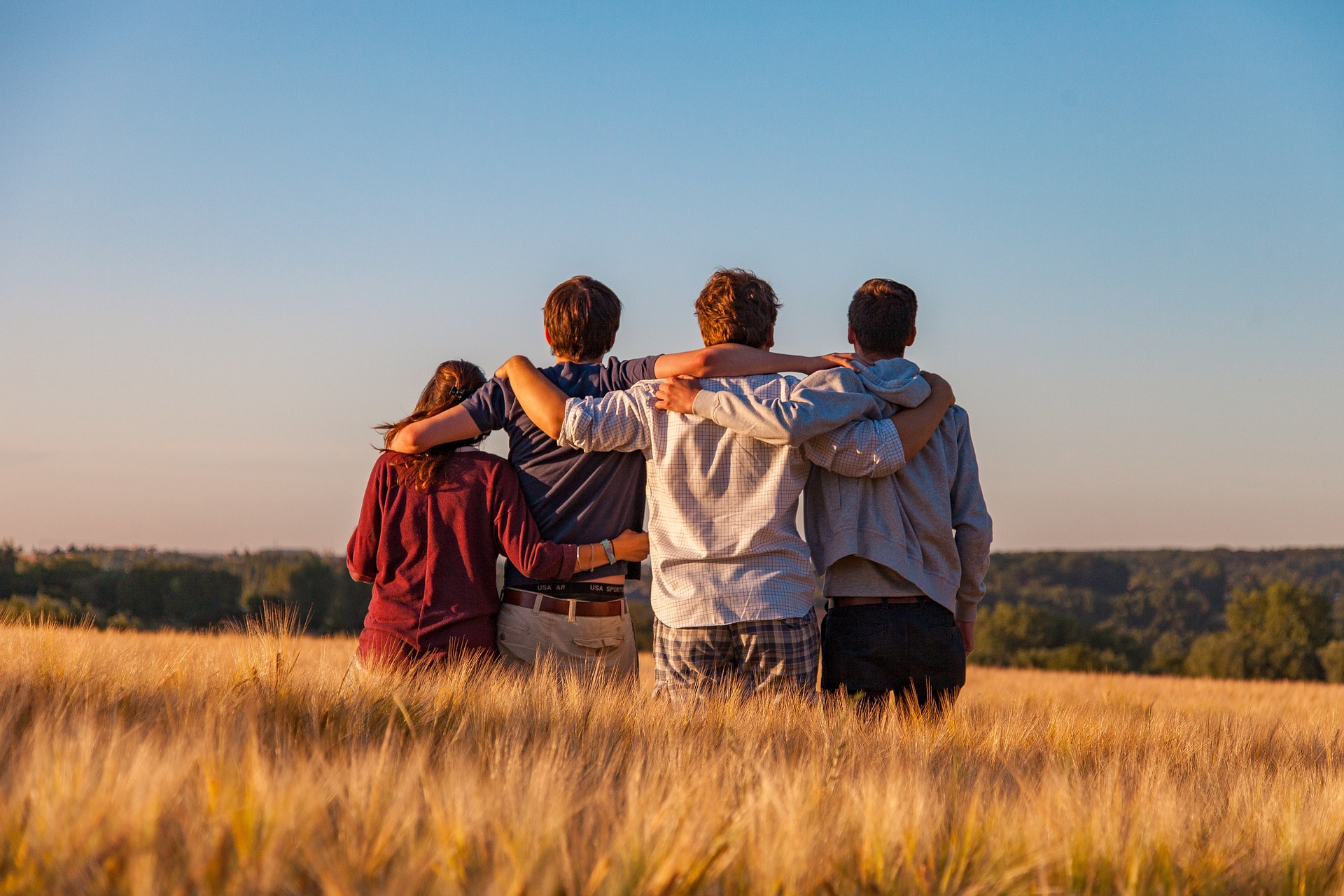 un groupe de 4 amis. Ils sont de dos, se tiennent pa la main et regardent le paysage